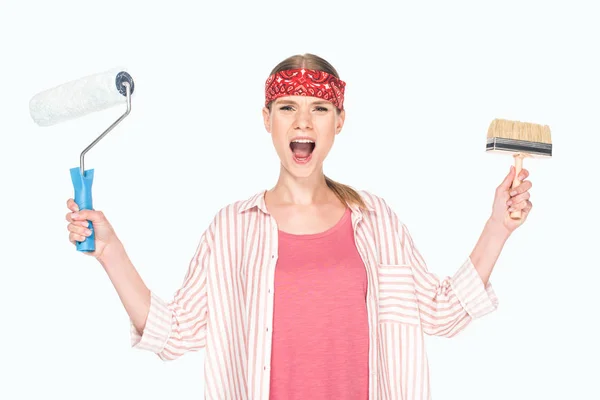 Screaming woman in headband holding paint roller and paint brush isolated on white background — Stock Photo