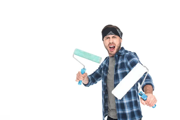 Jeune homme en colère dans le bandeau tenant des rouleaux de peinture isolés sur fond blanc — Photo de stock