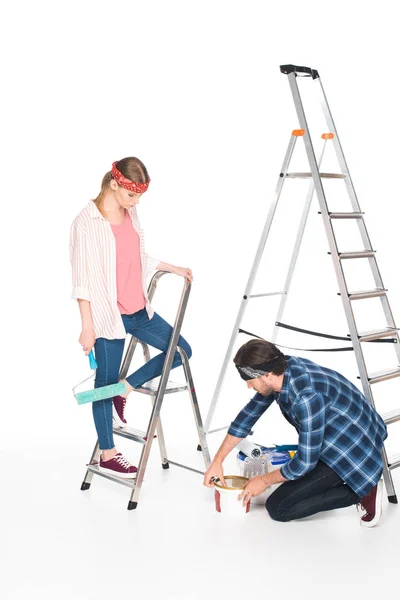 Hombre apertura pintura lata y novia de pie cerca en escalera con rodillo de pintura aislado sobre fondo blanco - foto de stock