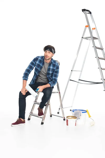 Hombre en diadema sentado en escalera con rodillo de pintura aislado sobre fondo blanco - foto de stock