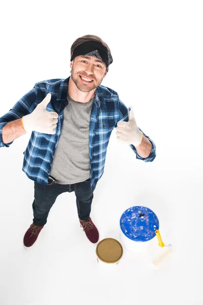 Vista de ángulo alto del hombre sonriente con guantes protectores haciendo un gesto hacia arriba con pulgares aislados sobre fondo blanco - foto de stock