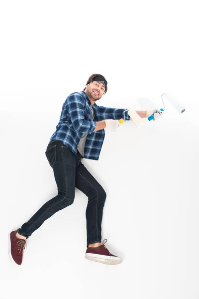 Vista lateral del hombre sonriente con guantes protectores con rodillos de pintura aislados sobre fondo blanco - foto de stock