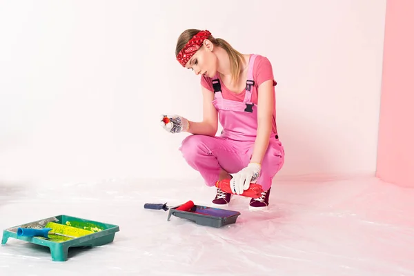 Mulher no trabalho geral e cabeça derramando líquido de garrafa em bandeja de rolo com rolo de pintura — Fotografia de Stock