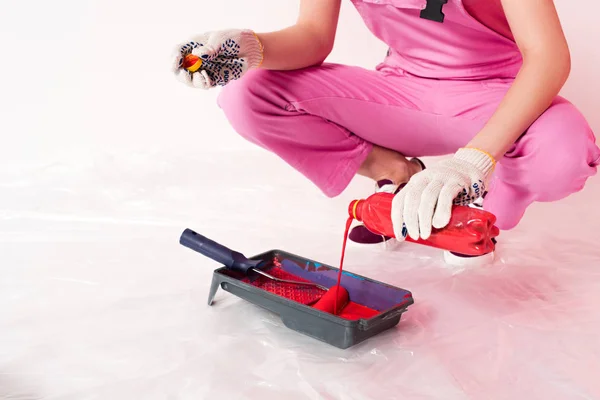 Immagine ritagliata della donna in guanti protettivi e liquido di versamento complessivo di lavoro dalla bottiglia nel vassoio del rullo — Foto stock