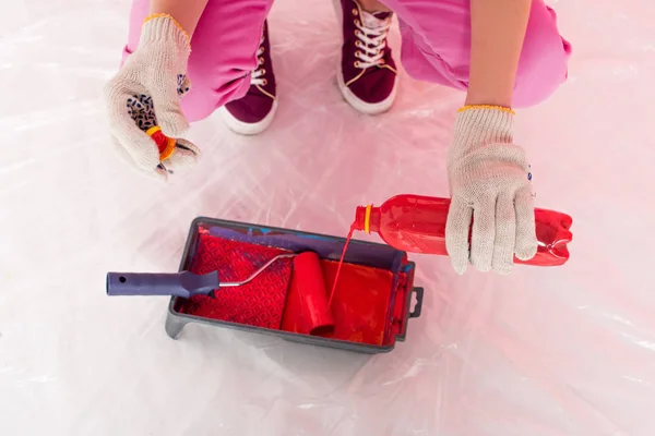 Cropped shot of woman in protective gloves pouring red paint from bottle into roller tray with paint roller — Stock Photo
