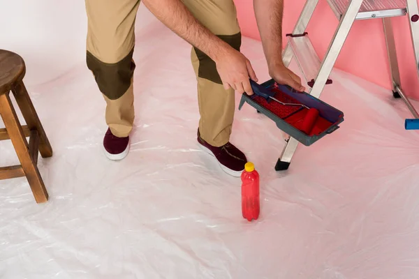 Imagen recortada del hombre en el trabajo en general sumergiendo el rodillo de pintura en la bandeja de rodillos - foto de stock