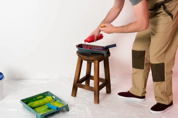 Colpo ritagliato di uomo nel lavoro generale versando vernice dalla bottiglia nel vassoio rullo sulla sedia — Foto stock