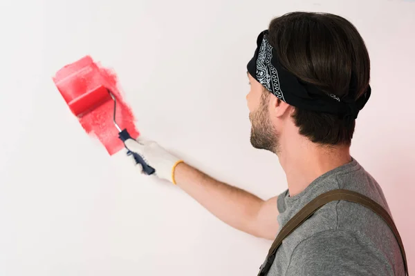 Visão traseira do homem na parede de pintura de faixa de cabeça em vermelho por rolo de pintura — Fotografia de Stock