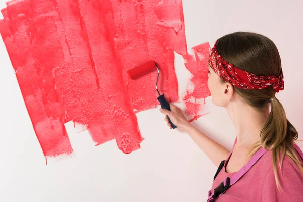 Back view of woman in headband painting wall in red by paint roller — Stock Photo