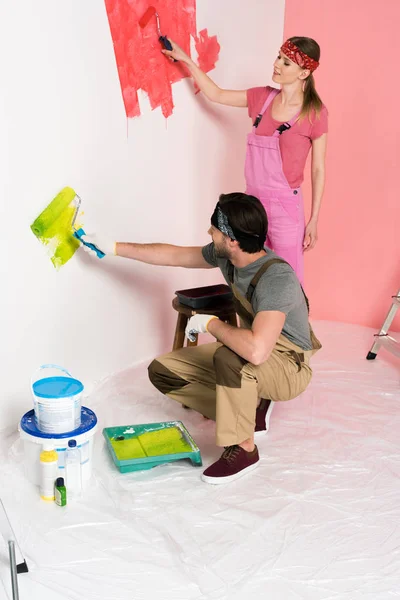 Jovem casal no trabalho macacão pintura parede por rolos de pintura — Fotografia de Stock