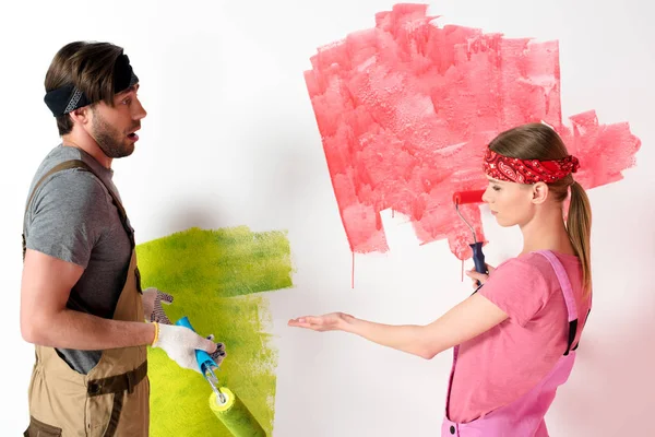 Jovem mulher apontando à mão na parede pintada para namorado enquanto ele fazendo gesto de encolher os ombros — Fotografia de Stock
