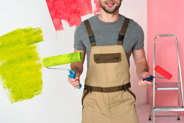 Imagen recortada del hombre en el trabajo en general con rodillos de pintura cerca de escalera - foto de stock