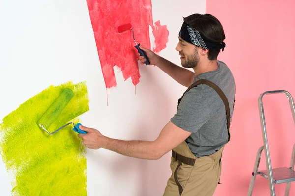 Vista laterale di uomo sorridente nel lavoro parete di pittura complessiva da due rulli di vernice — Foto stock
