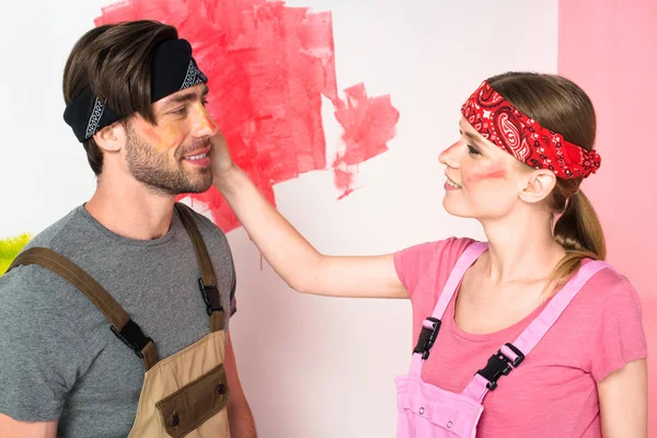 Visão lateral da jovem mulher no trabalho geral com rosto pintado tocando rosto namorado — Fotografia de Stock