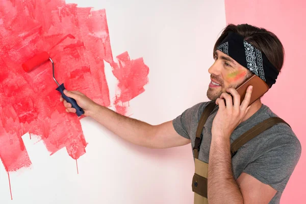 Sorridente homem falando no smartphone e pintura parede em vermelho por rolo de pintura — Fotografia de Stock