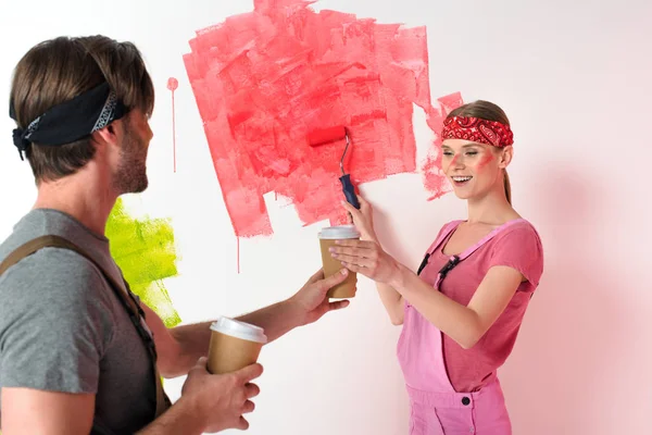 Молодий чоловік дає паперову чашку кави усміхненій дівчині, коли вона малює стіну — стокове фото