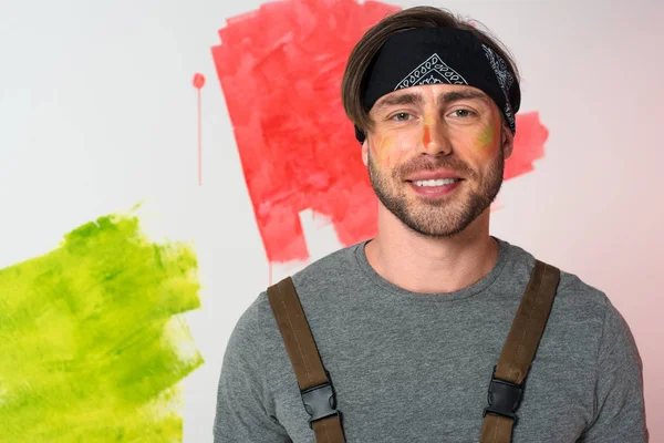 Portrait of smiling man with painted face in headband standing in front of painted wall — Stock Photo