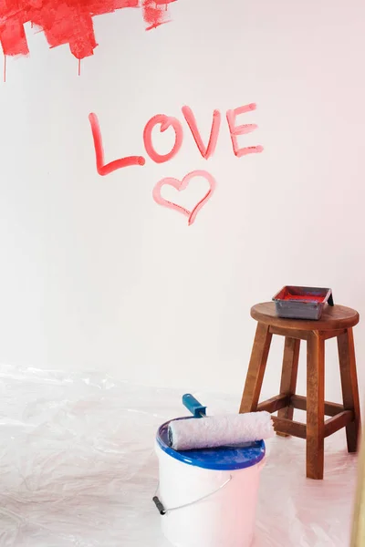 Wall with lettering love and heart symbol, paint tin with paint roller and chair with roller tray — Stock Photo
