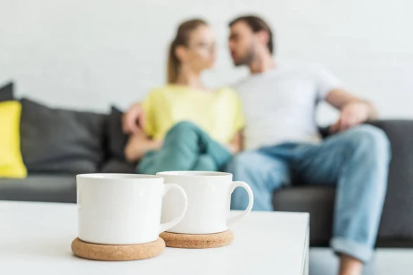 Крупным планом снимок двух чашек кофе и пары, сидящей на диване сзади — стоковое фото