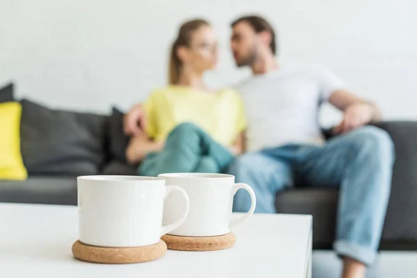 Close up shot of two coffee cups and couple sitting on sofa behind — Stock Photo