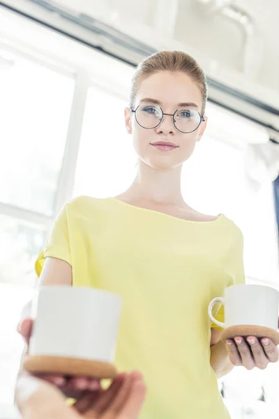 Low angle view of smiling woman in eyeglasses giving cup of coffee to boyfriend — Stock Photo