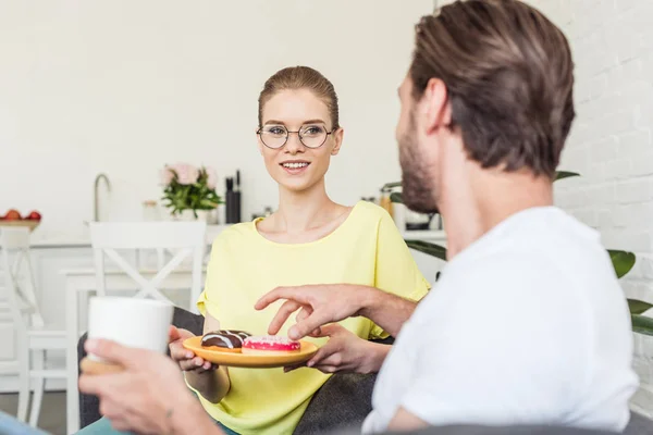 Uomo con tazza di caffè prendere ciambella dal piatto mentre la sua ragazza che lo tiene — Foto stock