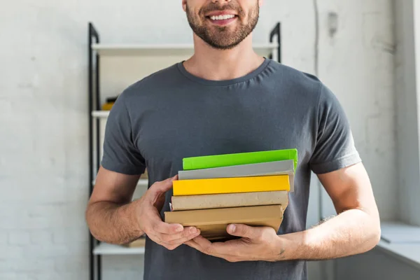 Image recadrée d'un homme souriant debout avec une pile de livres à la maison — Photo de stock