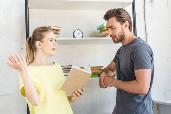 Seitenansicht einer lächelnden Frau, die mit der Hand gestikuliert und ihrem Freund Buch vorliest — Stockfoto