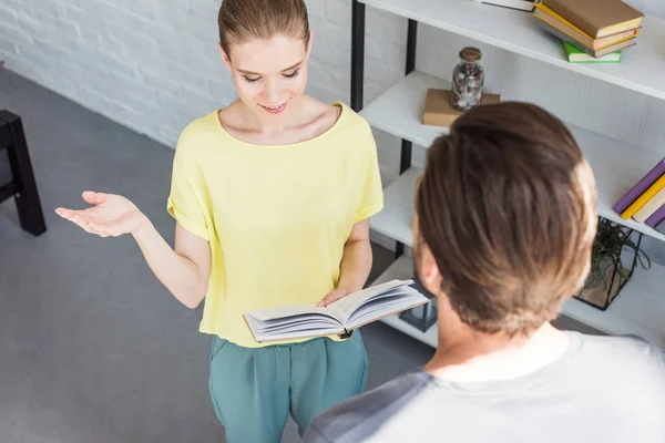 Hochwinkelaufnahme einer lächelnden Frau, die mit der Hand gestikuliert und ihrem Freund ein Buch vorliest — Stockfoto