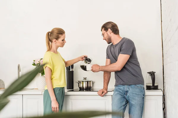 Vista lateral da mulher derramando café para namorado na cozinha — Fotografia de Stock
