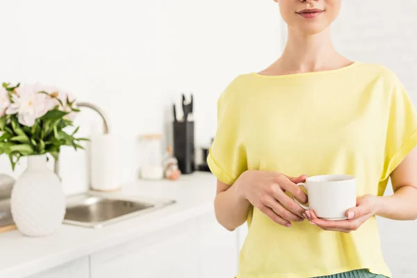 Обрезанный образ молодой улыбающейся женщины, держащей чашку кофе на кухне — стоковое фото