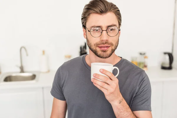 Retrato de jovem em óculos bebendo café na cozinha — Fotografia de Stock