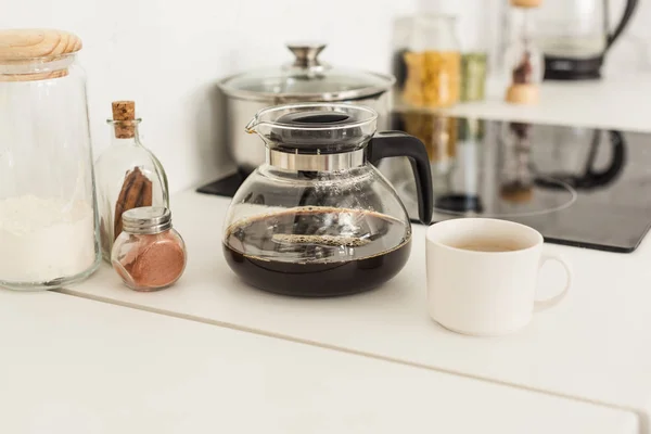 Vista da vicino di caffettiera, tazza e barattoli di vetro vicino stufa sul tavolo in cucina — Foto stock