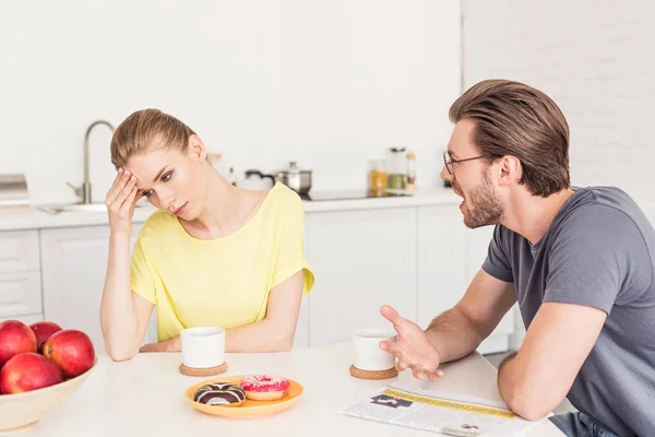 Angry man screaming at upset girlfriend while she sitting at table with breakfast — Stock Photo
