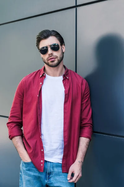 Elegante jovem modelo masculino em óculos de sol posando perto da parede preta — Fotografia de Stock