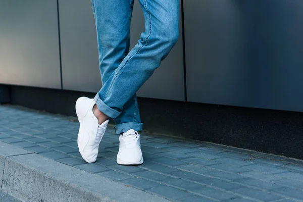 Imagem cortada de pernas masculinas elegantes em jeans e tênis brancos — Fotografia de Stock