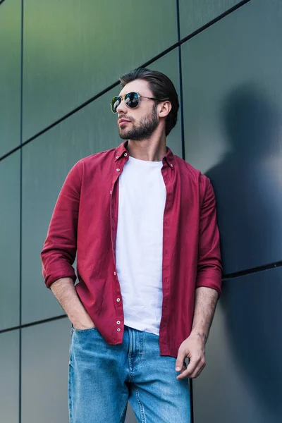 Vista angolo basso di elegante giovane uomo in occhiali da sole in piedi vicino alla parete — Foto stock