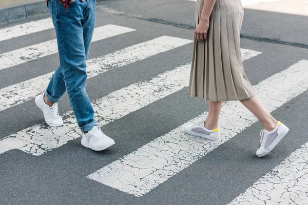 Cropped shot of stylish woman in skirt and man in jeans walking on crosswalk at city street — Stock Photo