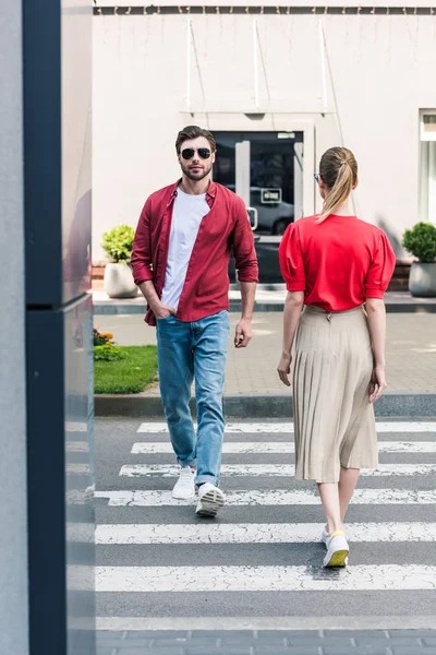 Rear view of stylish woman and man in sunglasses walking on crosswalk at city street — Stock Photo