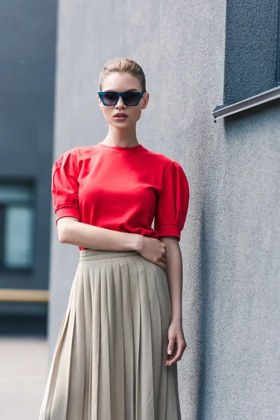 Modelo femenino con estilo en gafas de sol posando cerca del edificio - foto de stock