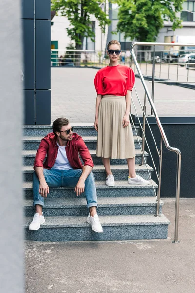 Young stylish couple of models in sunglasses on stairs at urban street — Stock Photo