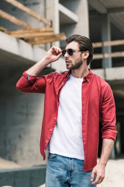 Jeune homme élégant ajuster les lunettes de soleil au bâtiment de construction — Photo de stock