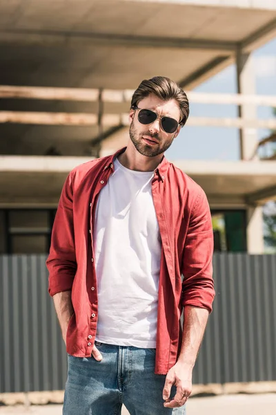 Portrait of young stylish man in sunglasses posing in front of construction building — Stock Photo