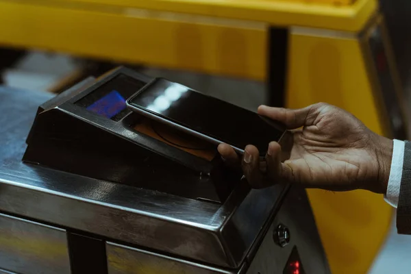 Vista recortada de mano masculina con smartphone pagando tarifa de transporte público - foto de stock