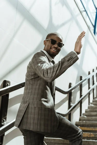 Lächelnder selbstbewusster Geschäftsmann winkt auf der Treppe stehend mit der Hand — Stockfoto