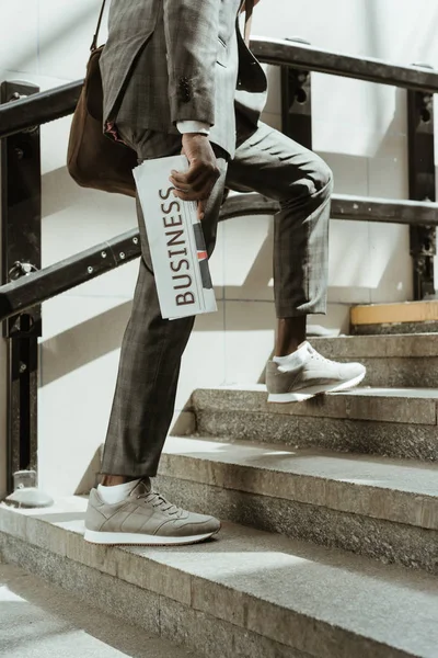 Cropped view of african american businessman with newspaper walking on stairs — Stock Photo