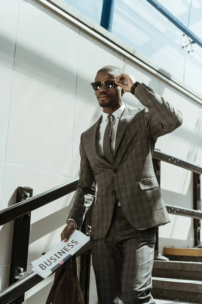 Stylish confident businessman with newspaper walking on stairs — Stock Photo