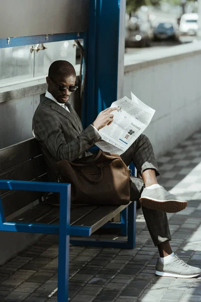 Giovane uomo d'affari afroamericano con giornale appoggiato sulla panchina — Foto stock