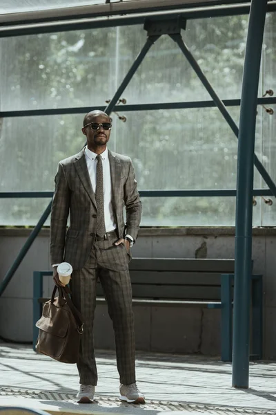 Uomo d'affari afroamericano vestito con valigetta e tazza di caffè in piedi sulla stazione dei trasporti pubblici — Foto stock