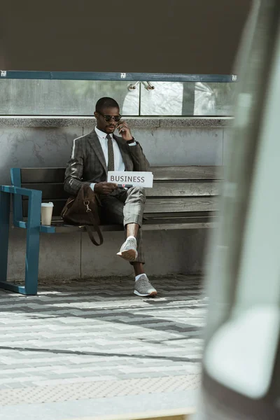 Homme d'affaires afro-américain en costume et tenant un journal reposant sur un banc — Photo de stock